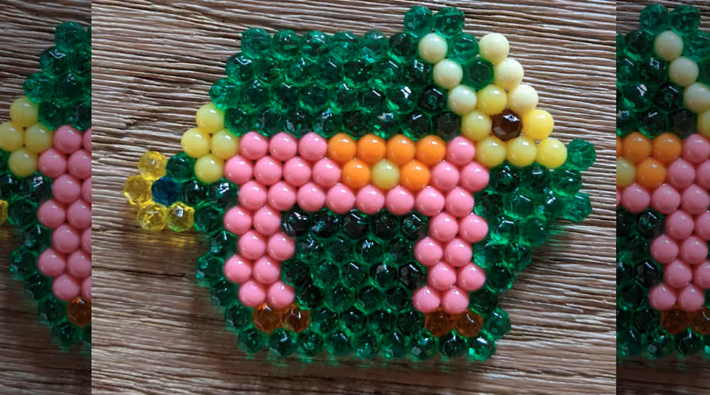 A green and pink beaded animal figure on a wood surface.