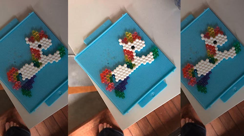 A unicorn made of white, red, blue and green Aquabeads on a blue tray.