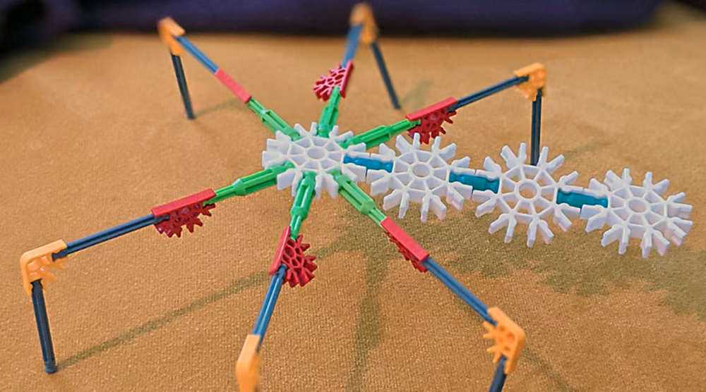 A white, green and red K&rsquo;nex star-shaped construction with legs, on a wooden table.