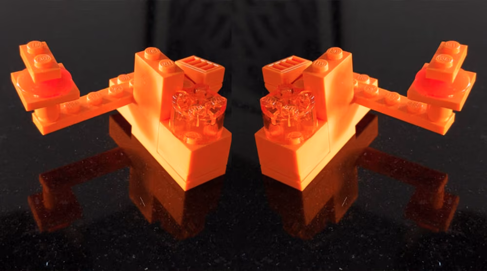 Two orange Lego pieces mirrored on a black glossy surface.