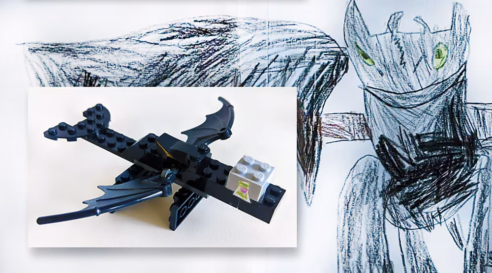 A child&rsquo;s black crayon drawing of a dragon with green eyes, with a photograph of a small black Lego dragon laid over it.